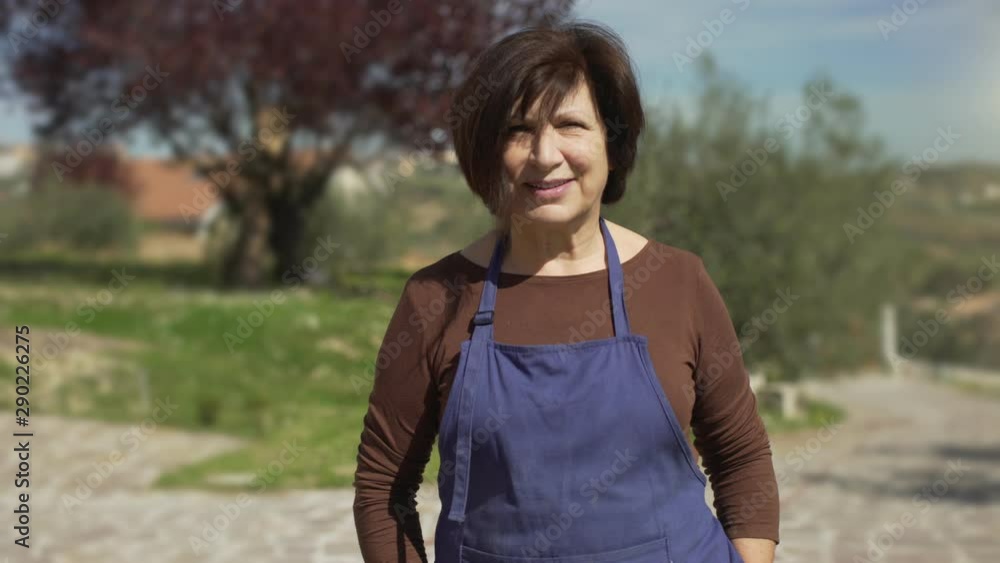 Portrait of happy beautiful mature worker woman with blue apron smiling at camera in an agricutural business in the garden. Portrait of happy beautiful mature worker woman with blue apron smiling at camera in an agricutural business in the garden.