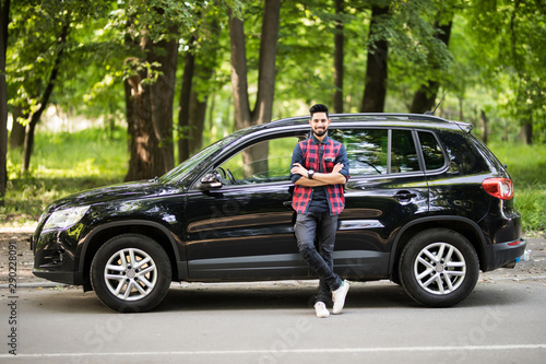 Young handsome indian man standing near his car on the road photo