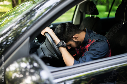 Tableau sur toile Closeup portrait tired young handsome man with short attention span, driving his car after long hours trip, trying to stay awake at wheel, isolated outside background