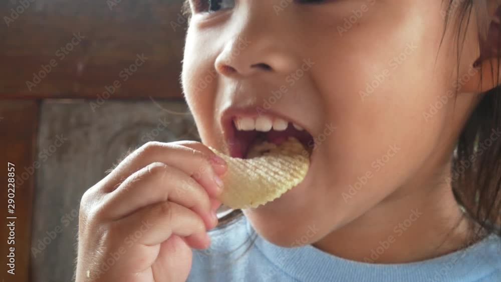 Happy Asian little child girl eating potato chips in the garden.