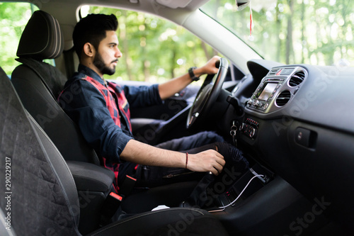 Young indian man in a business suit in the car changes gear
