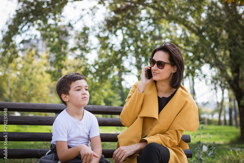 Mother talking on the phone while sitting with her son on park bench.