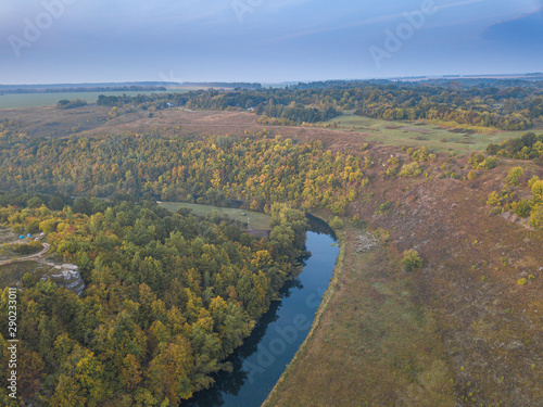 The turn of the river in valley with riversides covered by green forest and meadows under blue sky. Aerial panoramic view, drone shot. Russia, Vorgol river.