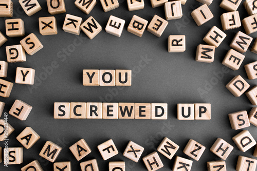 You screwed up - phrase from wooden blocks with letters,  doing something stupid concept, random letters around, grey background