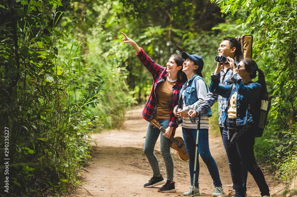 Group of Asian friends team adventure for hiking and camping in forest together. Family travel relaxation. Trekking and trail activity in wild life concept. Woman pointing at tree or sky. Copy space