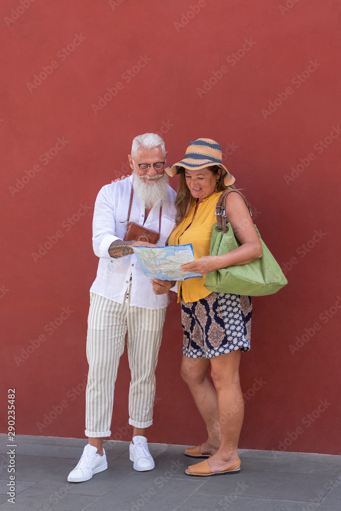 An elderly couple of tourist smiling and looking a city map. He has an old camera and she wears an hat. An elderly couple of tourist smiling and looking a city map. He has an old camera and she wears an hat.