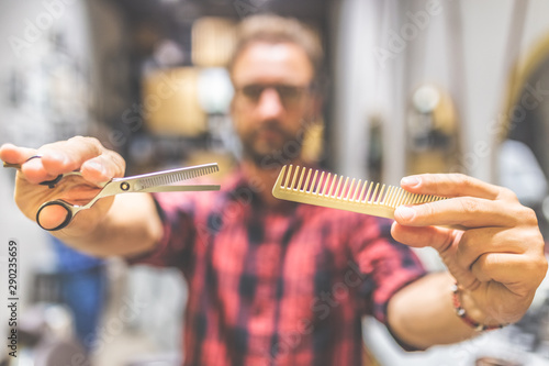Close up of fashionable hipster hairdresser holding comb and scissors.