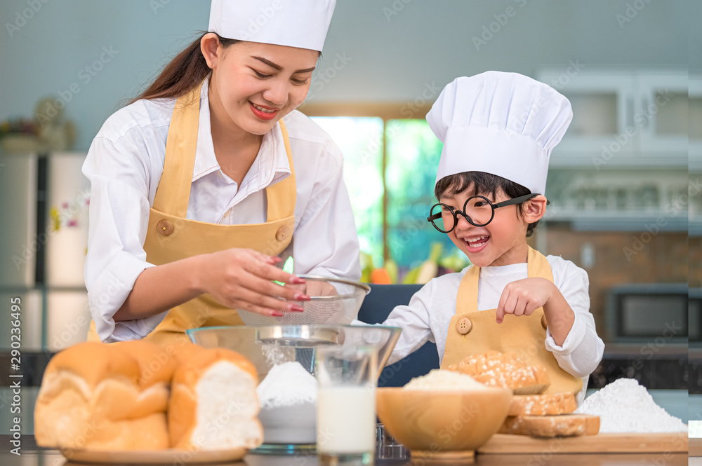 Cute little Asian boy and beautiful mother sifting dough flour with sifter sieve colander in home kitchen on table for prepare to baking bakery and cake. Thai kids playing with flour as chef funny Cute little Asian boy and beautiful mother sifting dough flour with sifter sieve colander in home kitchen on table for prepare to baking bakery and cake. Thai kids playing with flour as chef funny