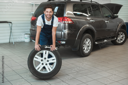 young handsome mechanic working in car service department fixing flat tire looks pleased