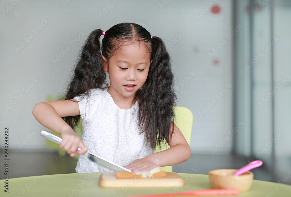 Portrait happy little child girl cooking at class room. Kid are using knife slicing bread on chopping wood board. Portrait happy little child girl cooking at class room. Kid are using knife slicing bread on chopping wood board.