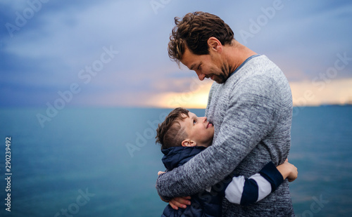 Obraz na plátně Father with small son on a walk outdoors standing on beach at dusk