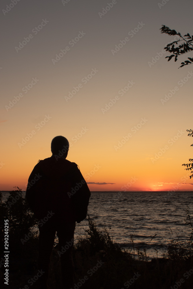 Silhouette of a man on the seashore in the rays of the setting sun