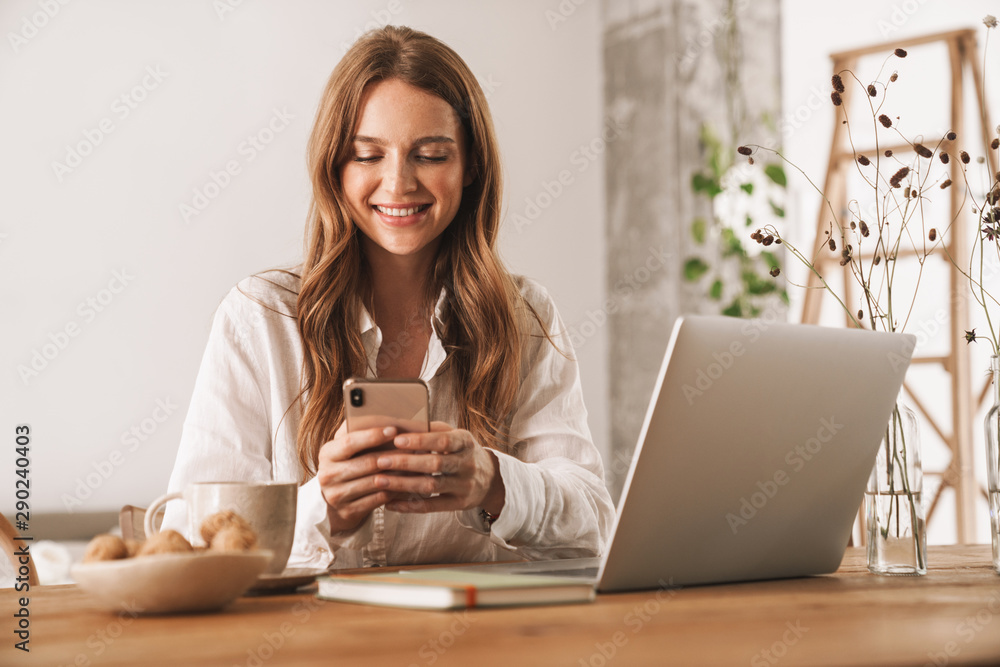 Business woman sit indoors in office using laptop computer and mobile phone. Business woman sit indoors in office using laptop computer and mobile phone.