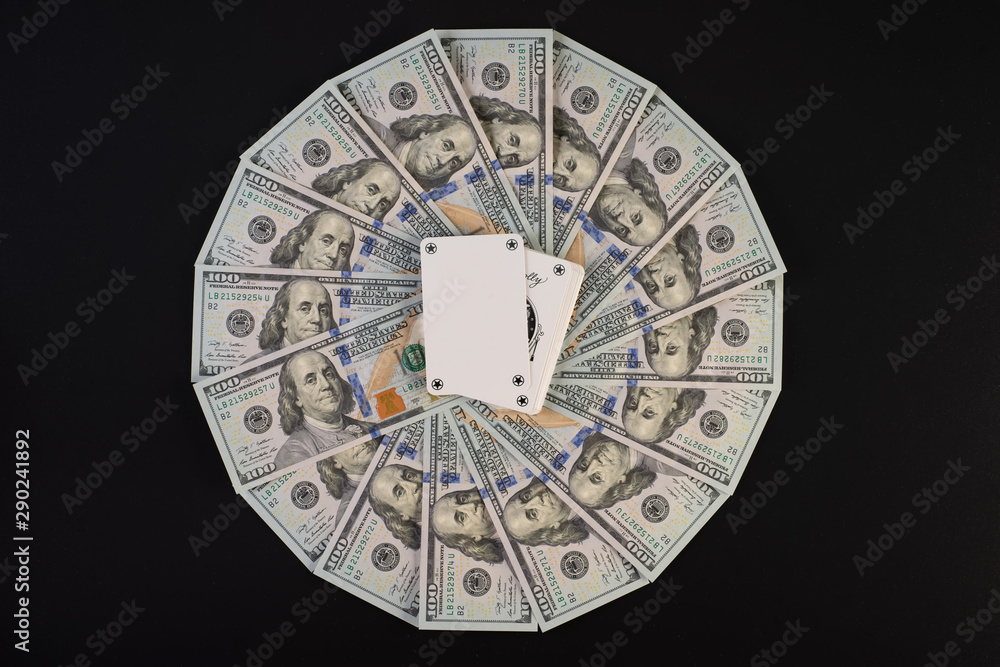 A pile of one hundred dollar bills laid out in a circle. In the middle of playing cards, on a black background