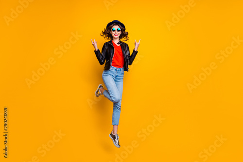 Full length photo of cheerful girl with curly hairstyle jump show horned sign rock on pank concert wear denim jeans good look isolated over yellow color background