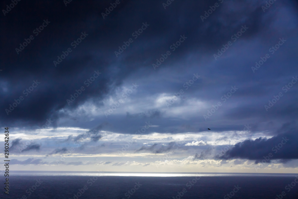 Dramatic sky over Atlantic Ocean coast near Sao Miguel Island, the largest island in the archipelago of the Azores, Portugal. Dark stormy clouds in the sky and strip of sunlight over the ocean surface Dramatic sky over Atlantic Ocean coast near Sao Miguel Island, the largest island in the archipelago of the Azores, Portugal. Dark stormy clouds in the sky and strip of sunlight over the ocean surface