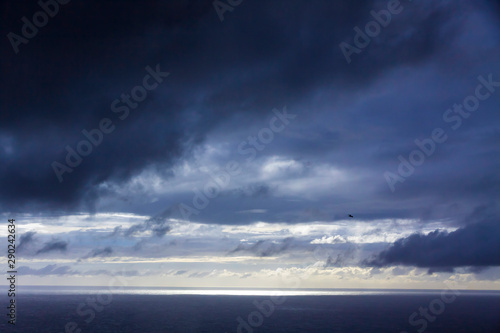 Dramatic sky over Atlantic Ocean coast near Sao Miguel Island, the largest island in the archipelago of the Azores, Portugal. Dark stormy clouds in the sky and strip of sunlight over the ocean surface