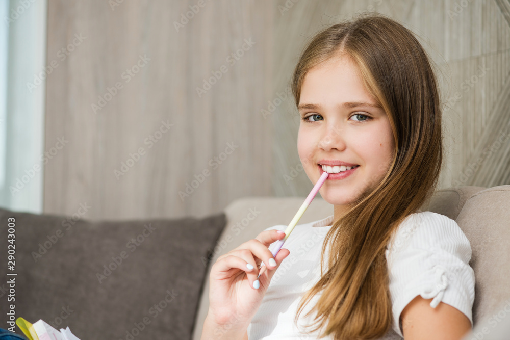 Smiling school girl sit on home couch with pencil Smiling school girl sit on home couch with pencil