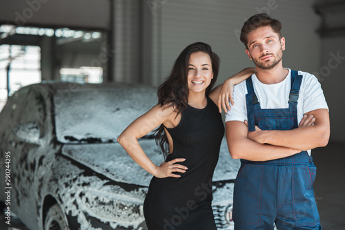 young handsome man wearing uniform and beautiful woman client standing in car wash station satisfied with excellent service photo