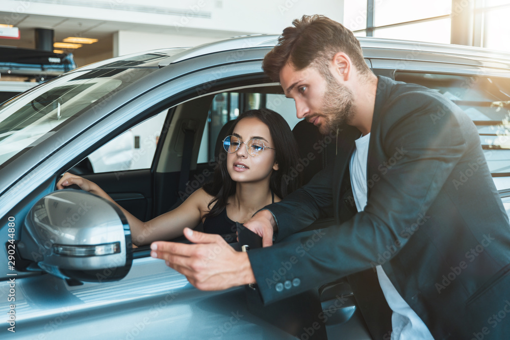 handsome man manager consulting young beautiful woman client while choosing new car in dealership center handsome man manager consulting young beautiful woman client while choosing new car in dealership center