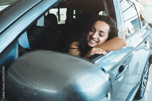 young beautiful woman sitting in new vehicle checking car interior while choosing new car in dealership center