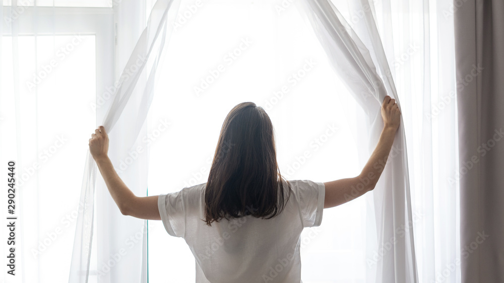 Woman waking up and standing near window - obrazy, fototapety, plakaty 
