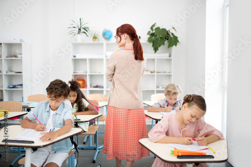 Teacher walking between desks while children writing test