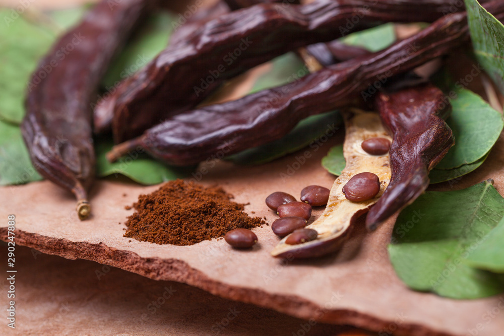 Obraz premium Carob. Organic carob pods with seeds and leaves on tree bark table. Healthy eating, food background.