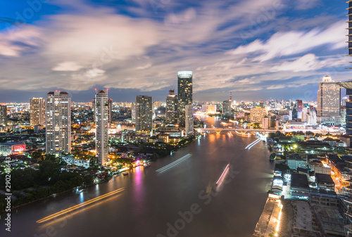 Bangkok cityscape rooftop view at night over Chao Phraya River waterfront with hotel buildings in central business district (CBD) and tourist boats transportation