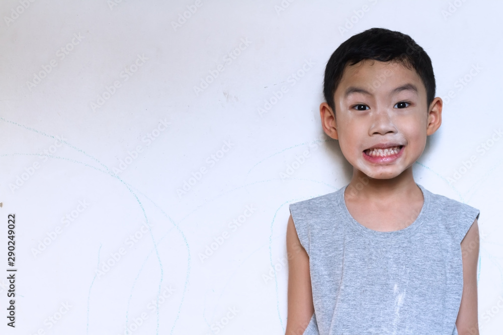 Asian black hair naughty boy age 5 years old wear gray t-shirt use baby powder on his face and say cheese for smiling with white cement wall background. Asian black hair naughty boy age 5 years old wear gray t-shirt use baby powder on his face and say cheese for smiling with white cement wall background.