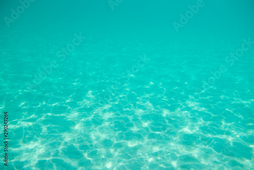 Underwater. Sun glare at the bottom of the seat. Waves underwater and rays of sunlight shining through. Deep turquoise blue sea. Ocean. Transparent water and light at sand. © Khorzhevska