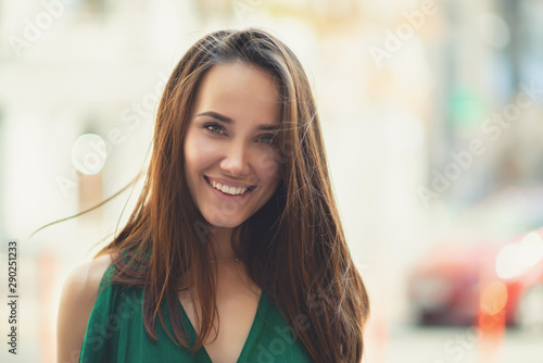 Young pretty likable cheerful woman posing summer city outdoor. Beautiful self-confident girl dressed in emerald-colored jumpsuit with long brown hair walking street enjoing her life, urban lifestyle photo