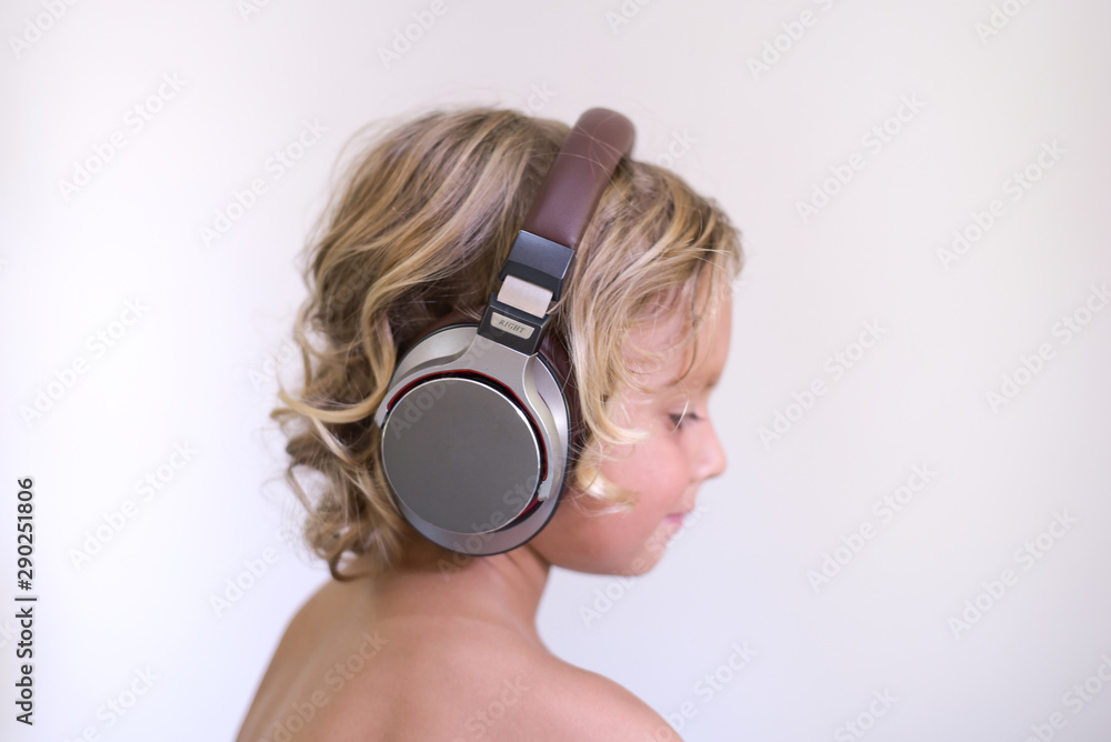 Fototapeta premium Happy smiling little child enjoys listens to music in headphones.Cute blond kid boy 4 years old on white background. People childhood lifestyle concept.Vivid and fun emotions. side view.