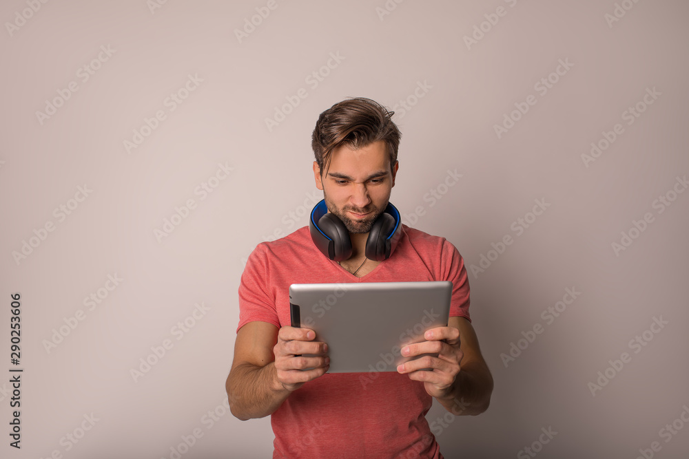 Young man having an exciting online game via portable touch pad computer while standing isolated in studio against grey wall with copy space background for promotional content Young man having an exciting online game via portable touch pad computer while standing isolated in studio against grey wall with copy space background for promotional content