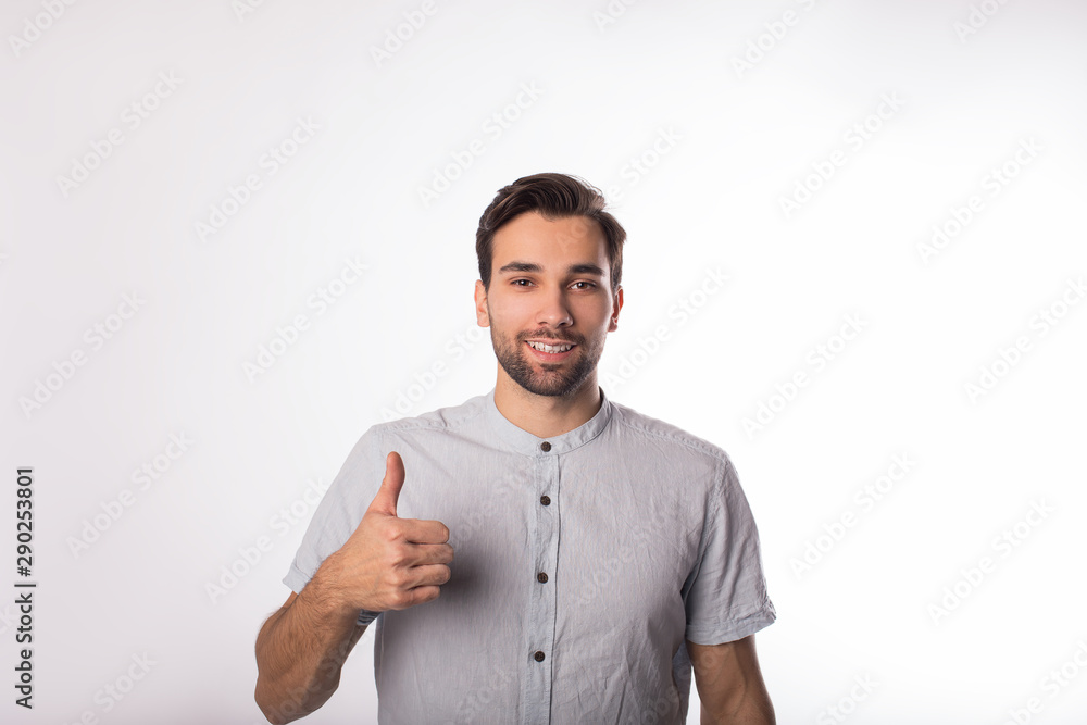 Portrait of a young beautiful bearded caucasian man business worker shows hand sign well and looking in camera while standing isolated in studio Portrait of a young beautiful bearded caucasian man business worker shows hand sign well and looking in camera while standing isolated in studio