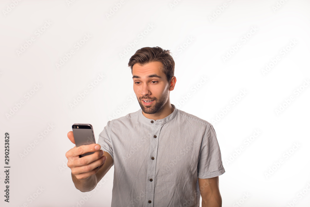 Handsome beaded man reading shocked good news on mobile phone while standing isolated in studio Handsome beaded man reading shocked good news on mobile phone while standing isolated in studio