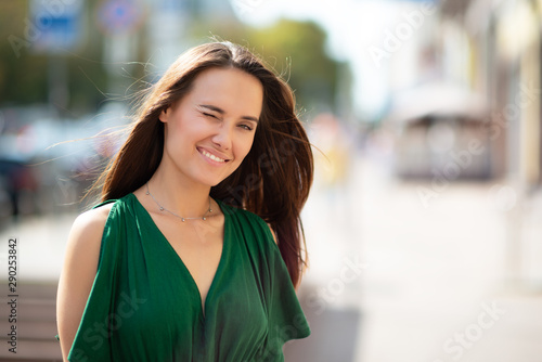 Young pretty likable cheerful woman posing summer city outdoor. Beautiful self-confident girl dressed in emerald-colored jumpsuit with long brown hair walking street enjoing her life, urban lifestyle photo
