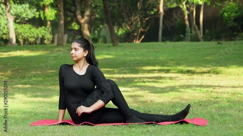A young girl practicing Vakrasana yoga asana in a park.  photo