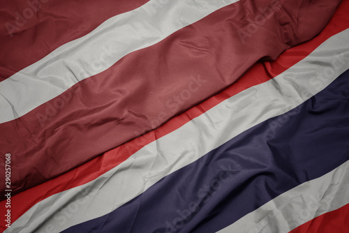 waving colorful flag of thailand and national flag of latvia.