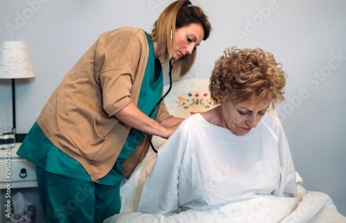 Female caregiver auscultating senior woman at home photo