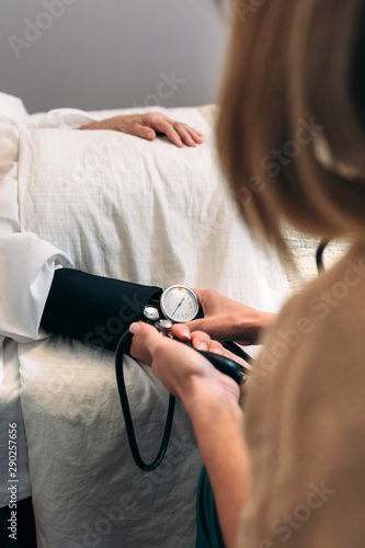 Unrecognizable female caregiver checking blood pressure to a senior woman at home