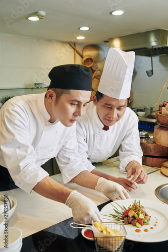 Two chefs working in team they standing at the table and decorating the prepared dish at the restaurant