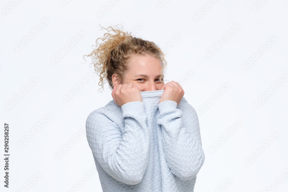 young caucasian curly woman hiding face under blue sweater being shy. Studio shot. young caucasian curly woman hiding face under blue sweater being shy. Studio shot.