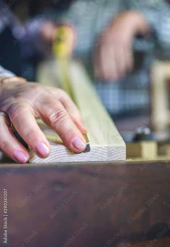 Detail of hand of senior carpenter measuring in a carpentry workshop. Selective focus on man in background