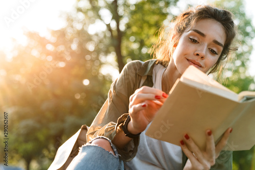 Image of young woman smiling and reading book in green park photo