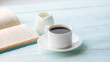 Cup of black coffee and book on a blue wooden background. Selective focus. Copy space. Horizontal frame.