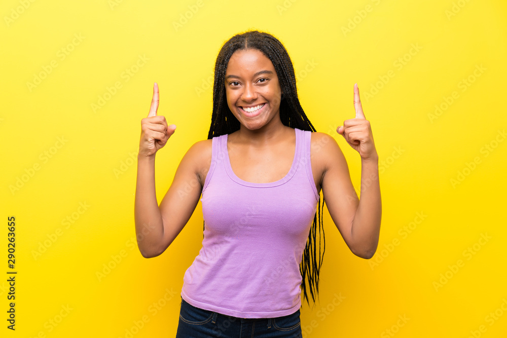 African American teenager girl with long braided hair over isolated yellow wall pointing up a great idea African American teenager girl with long braided hair over isolated yellow wall pointing up a great idea