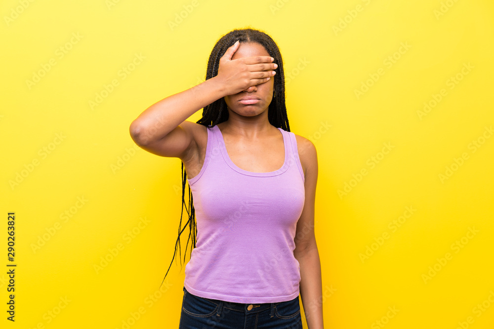 African American teenager girl with long braided hair over isolated yellow wall covering eyes by hands. Do not want to see something African American teenager girl with long braided hair over isolated yellow wall covering eyes by hands. Do not want to see something