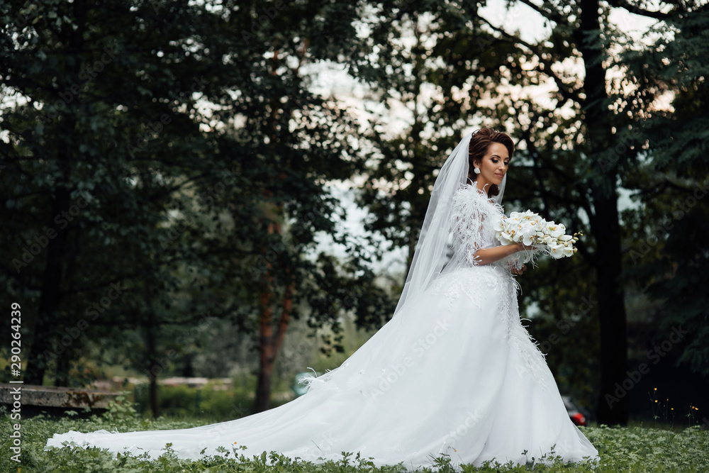 Fototapeta premium Bride holding a bouquet of white orchids. Beautiful woman. Wedding bouquet in bride's hands. Beautiful bride in white dress in the garden. Beautiful woman with professional make up and hair style.