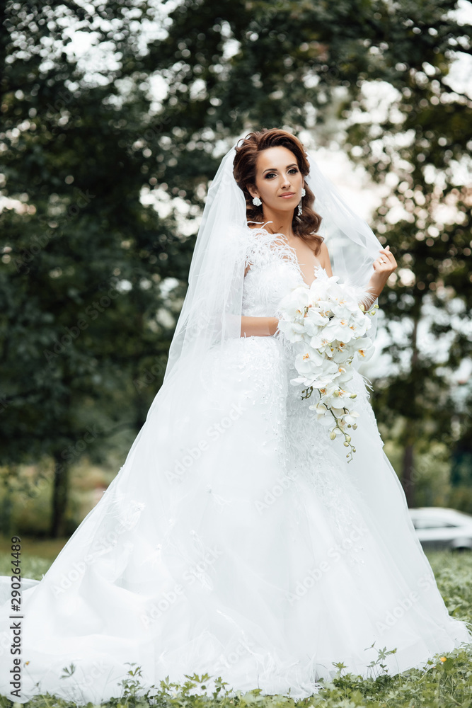 Bride holding a bouquet of white orchids. Beautiful woman. Wedding bouquet in bride's hands. Beautiful bride in white dress in the garden. Beautiful woman with professional make up and hair style.